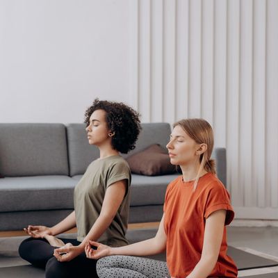 A person sitting calmly on a yoga mat with eyes closed in a well-lit room.
